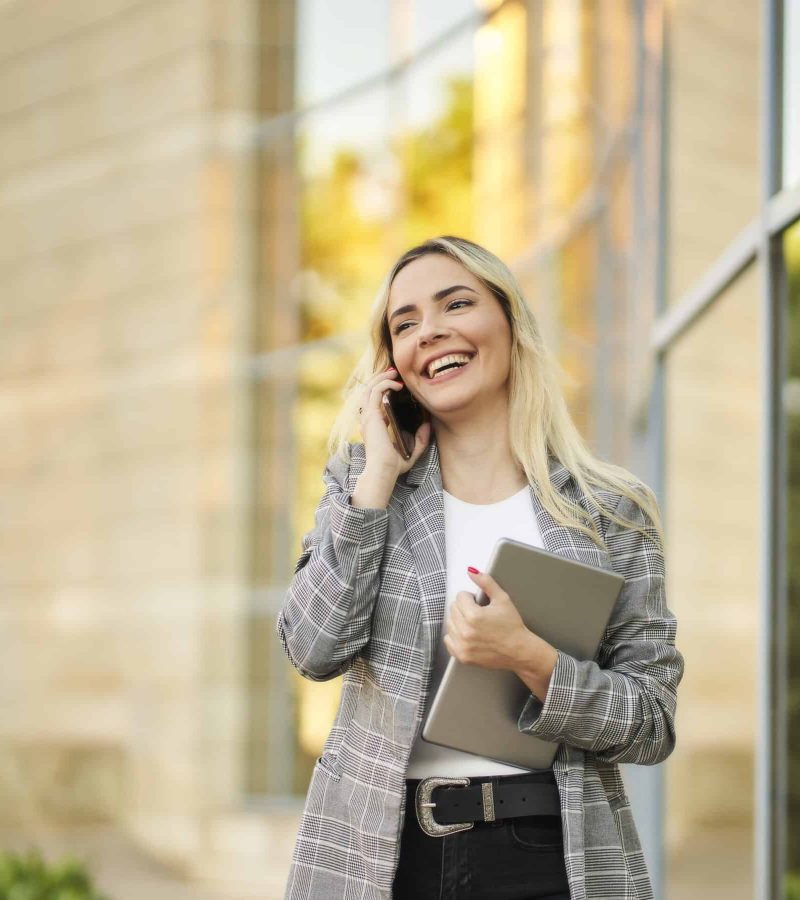 Young businesswoman talking on smart phone outside office